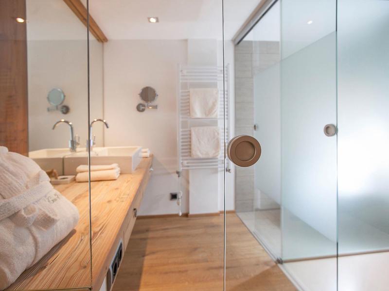 Nowoczesna łazienka z drewnianymi akcentami, szklaną prysznicem i białymi ręcznikami.