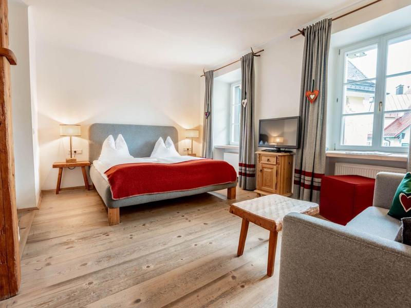 Jasno urządzone pokój hotelowy z łóżkiem podwójnym, częścią wypoczynkową, TV i drewnianą podłogą.