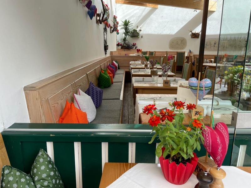 Przytulna jadalnia z kolorowymi poduszkami i roślinami w jasnej, zadaszonej przestrzeni.