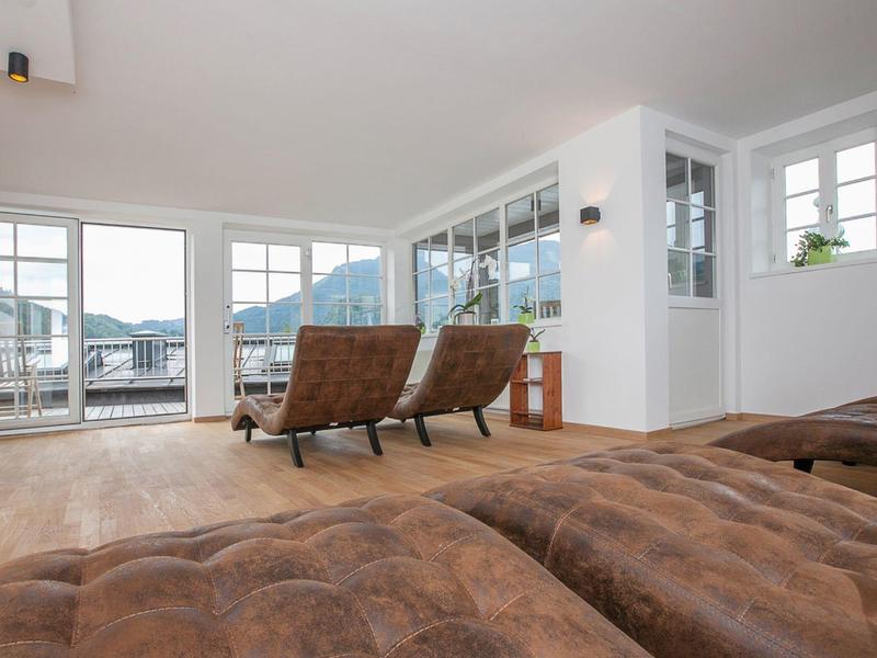 Jasny salon z dużymi oknami, widokiem na góry i skórzanymi fotelami na drewnianej podłodze.