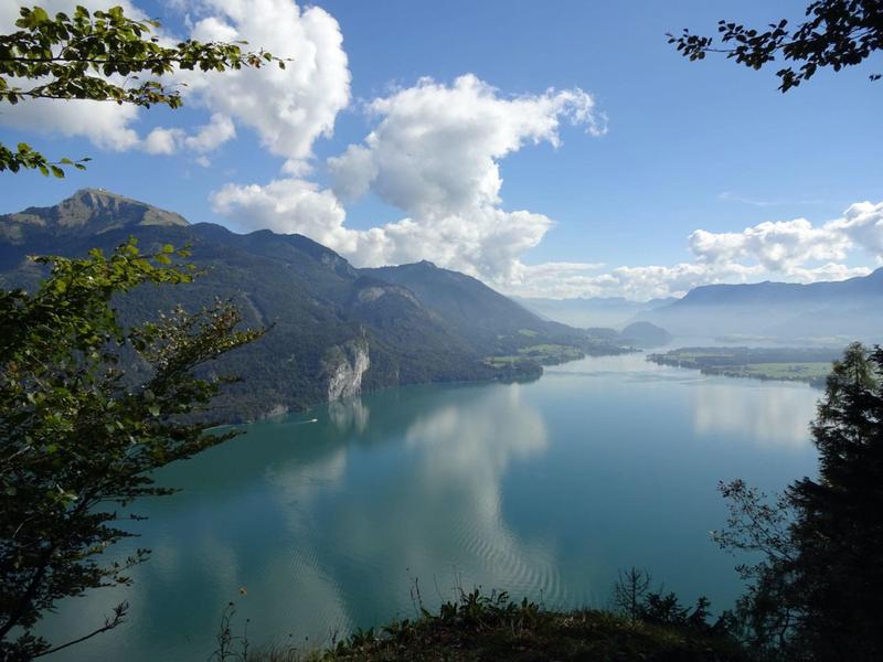 Widok na spokojne jezioro otoczone górami pod częściowo zachmurzonym niebieskim niebem.