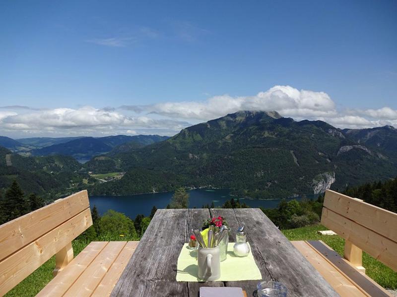 Drewniany stół z dwiema ławkami na tarasie z widokiem na góry i jezioro pod czystym niebem.