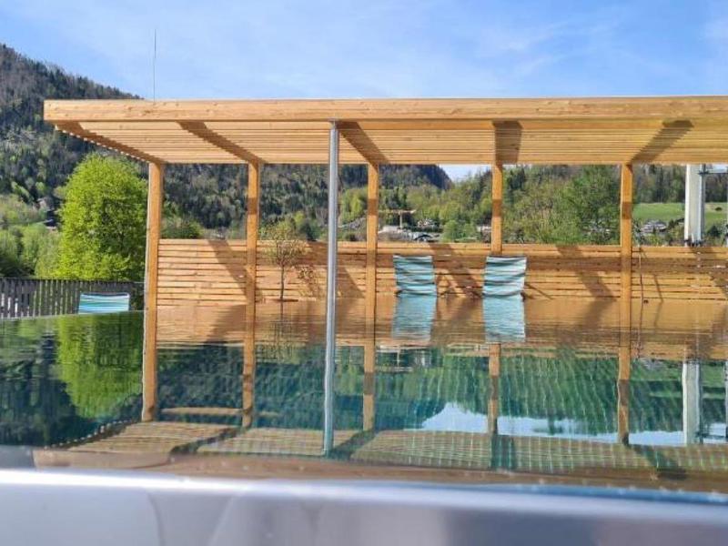 Nowoczesny basen na zewnątrz z drewnianą pergolą, otoczony górami i zieloną przyrodą.