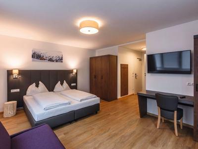 Modern hotel room with double bed, desk, TV, and wooden furniture.