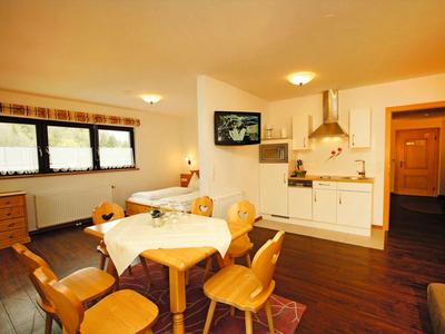 Cozy hotel room with dining tables, chairs, and a kitchen area with light wood.