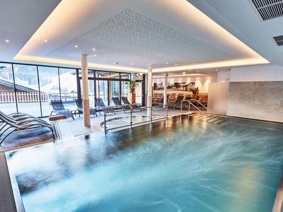 Indoor pool with large windows and modern lounge chairs in a hotel.