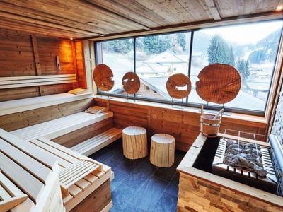 Bright sauna with wood paneling, large windows, and round wooden stools.