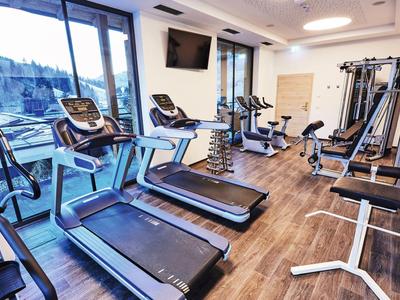 Modern gym with treadmills, workout machines, large windows, and wooden flooring.