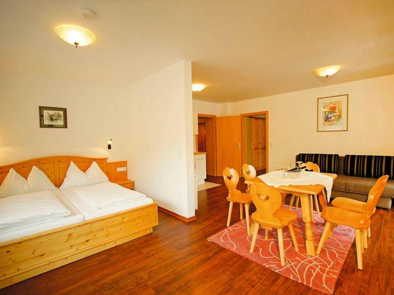 Brightly furnished hotel room with double bed, dining table, and seating area on wooden floor.