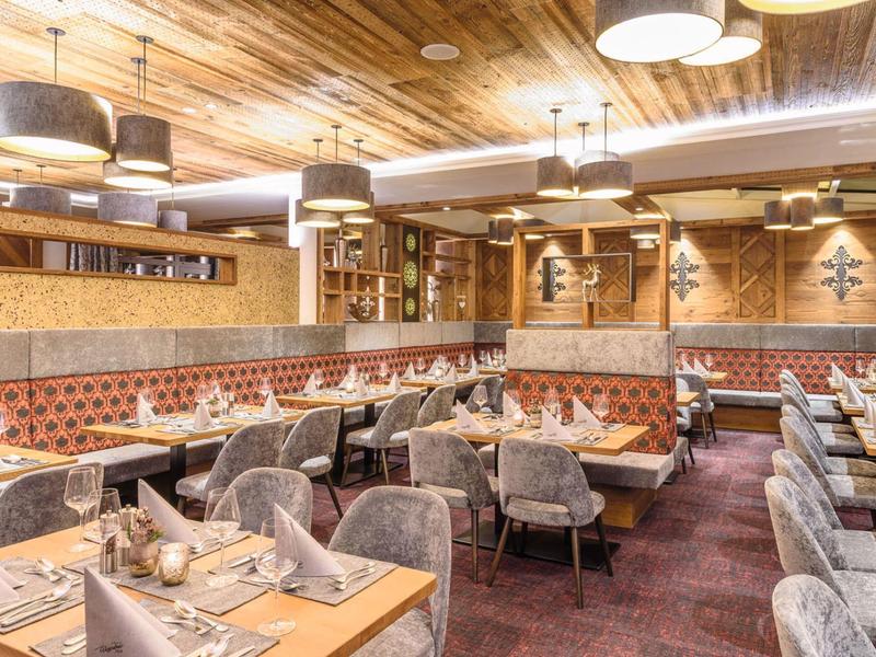 Elegant restaurant with gray chairs, wooden tables, and warm lighting.