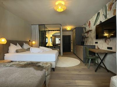 Camera d'hotel moderna con letto matrimoniale, pavimento in legno e area lavoro con TV a schermo piatto.