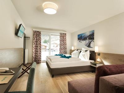 Helles Hotelzimmer mit Doppelbett, Sofa, Schreibtisch und Blick auf verschneite Berge.