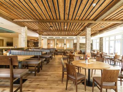 Geräumiger, moderner Speisesaal mit Holzboden, Holzdecken und Tischen mit Stühlen, hell beleuchtet.