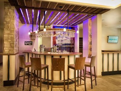 Moderner Hotelbarbereich mit Holzstühlen und beleuchtetem Tresen unter Deckenbeleuchtung.