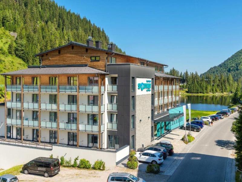 Modernes Hotelgebäude in einer Berglandschaft mit Parkplätzen und Außenpool