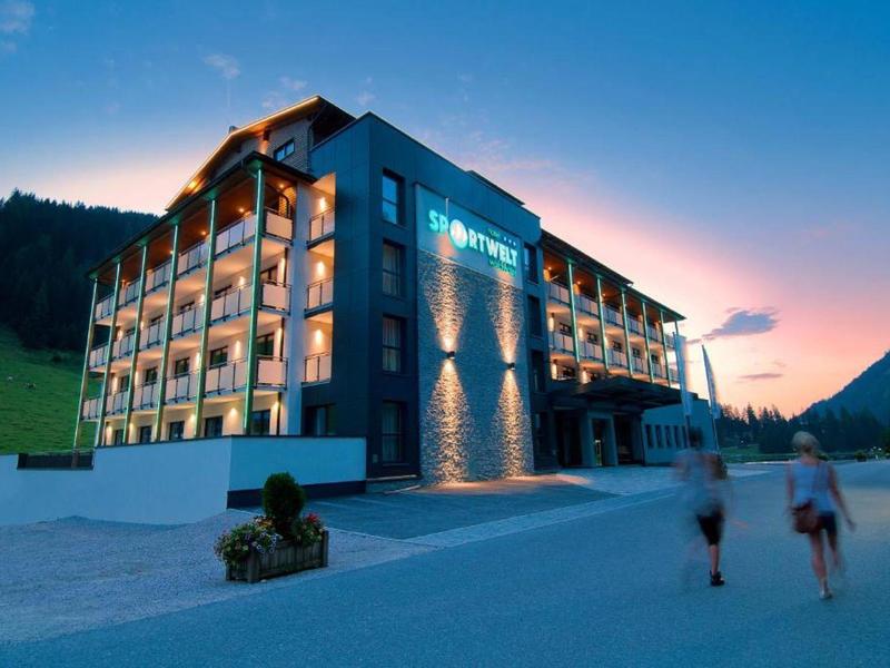 Modernes Hotelgebäude in den Bergen bei Sonnenuntergang mit beleuchteten Balkonen.