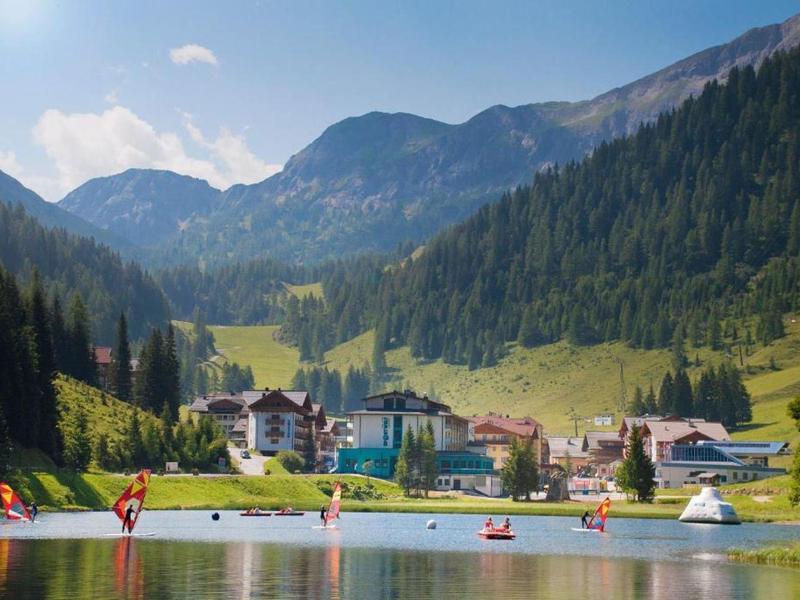 Bergdorf am See mit Segelbooten und Wald auf sanften Hügeln unter blauem Himmel