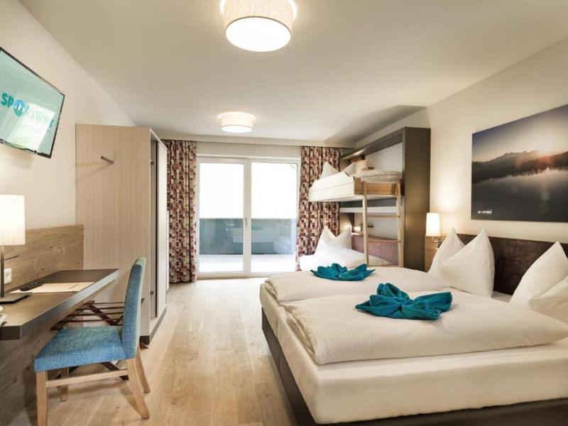 Modernes Hotelzimmer mit Doppelbett, Etagenbett, Balkon und Schreibtisch.