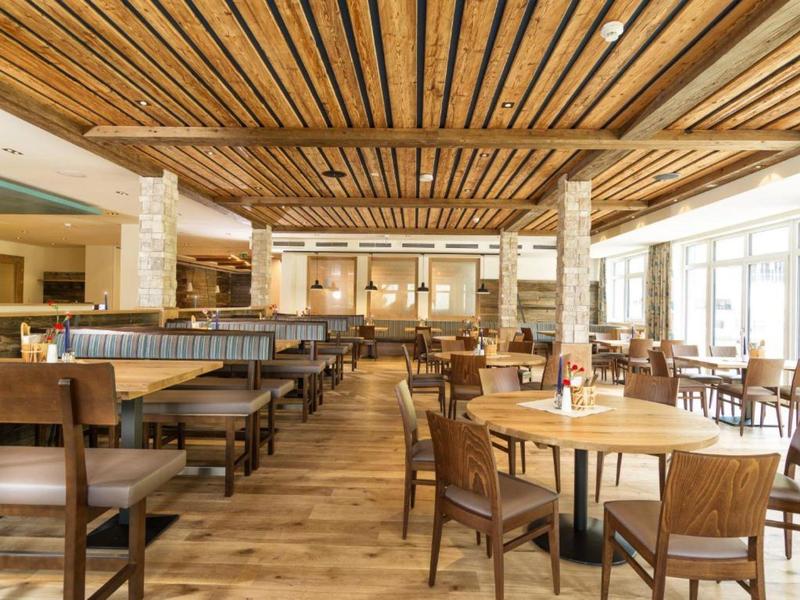 Geräumiger Restaurantbereich mit Holzbalkendecke, Holztischen und Stühlen sowie großen Fenstern.