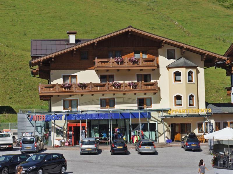 Mehrstöckiges Hotelgebäude mit Holzverkleidung und umliegenden Parkplätzen in Berglandschaft.