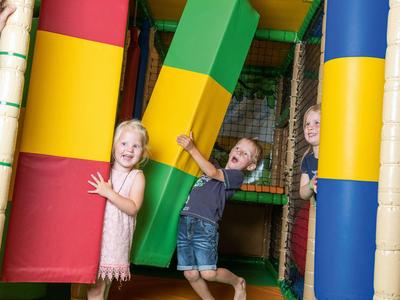 Kinder spielen in einem bunten Indoor-Spielbereich mit großen weichen Blöcken.