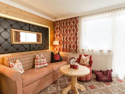 Gemütliche Sitzecke mit Ecksofa, rundem Tisch und großen Fenstern in warmem Hotelzimmer.