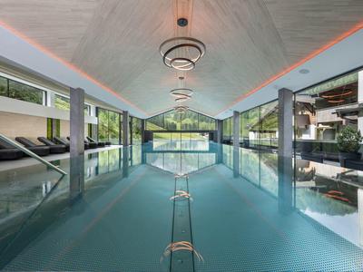 Moderner Indoor-Pool mit großer Glasfront und Liegestühlen an den Seiten.