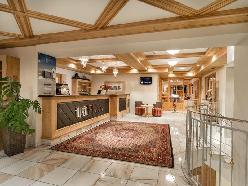 Großer Hotellobby-Bereich mit einem Empfangstresen, dekorativem Teppich und holzverkleidetem Deckenbalken.