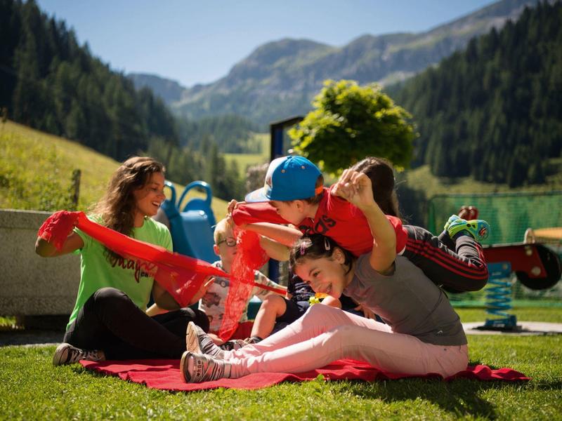 Familie mit zwei Kindern sitzt auf einer Decke in der Natur bei Bergkulisse.