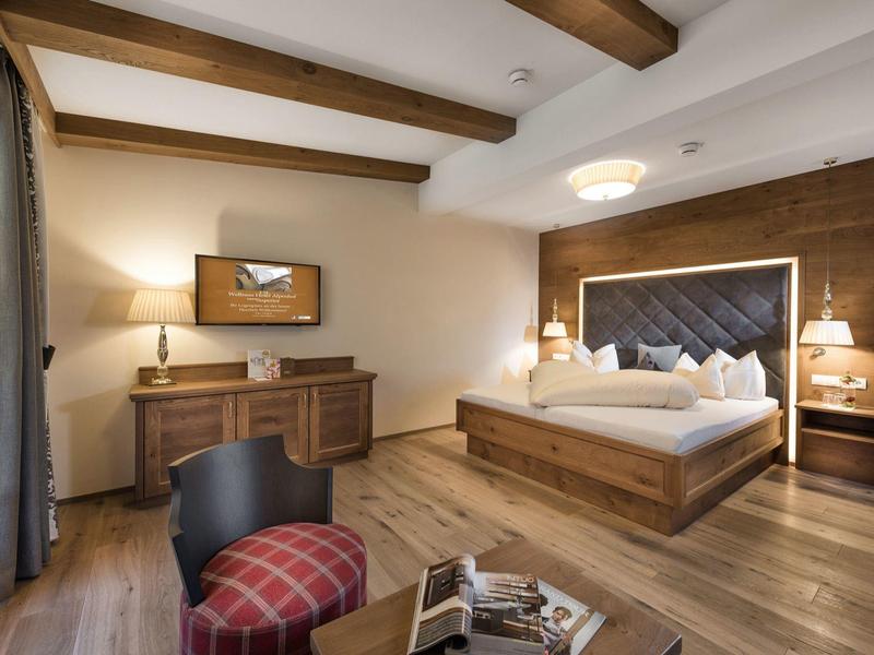 Modernes Hotelzimmer mit Holzboden, Doppelbett, schräger Kopfteilwand und Schreibtisch mit Fernseher.