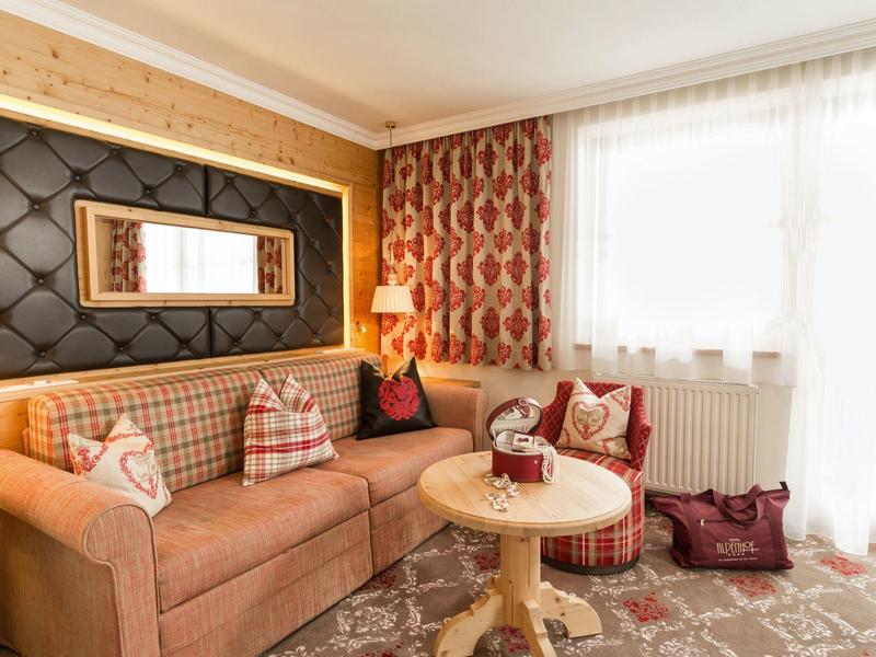 Gemütliche Hotellounge mit brauem Ecksofa, runden Tisch und warmen Vorhängen an großem Fenster.