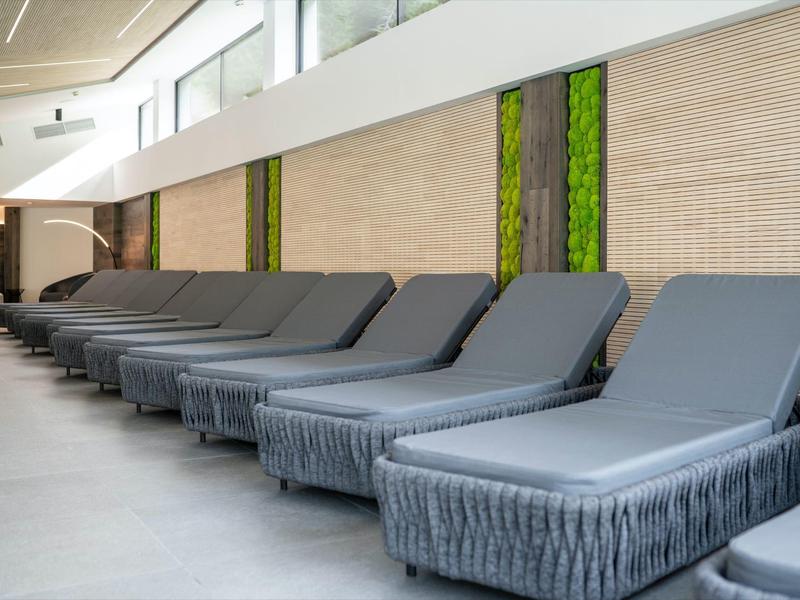 Mehrere graue Liegen mit Kissen in einer modernen, hellen Lounge mit grün dekorierten Wänden.