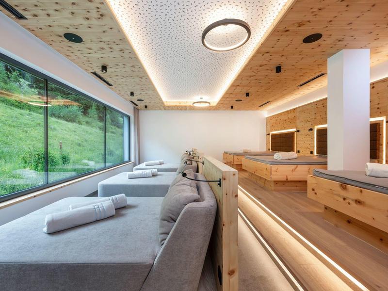 Moderner Ruheraum mit grauen Liegen, großen Fenstern und Holzverkleidung in einem Hotel.