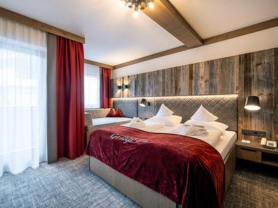 Modernes Hotelzimmer mit Doppelbett, Holzwand, roten Vorhängen und weicher Beleuchtung.