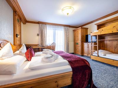 Gemütliches Hotelzimmer mit Holzmöbeln, großem Bett, Fernseher und Fenster mit Vorhängen.