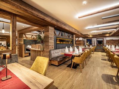 Gemütlicher Holzinnenraum eines Restaurants mit Tischen, Stühlen und warmem Licht.