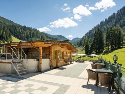 Terrasse mit Tischen und Stühlen neben einem Holzgebäude in einer Berglandschaft