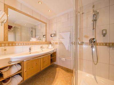 Helles Badezimmer mit Duschkabine, Doppelwaschbecken und Holzschränken unter der Arbeitsplatte.