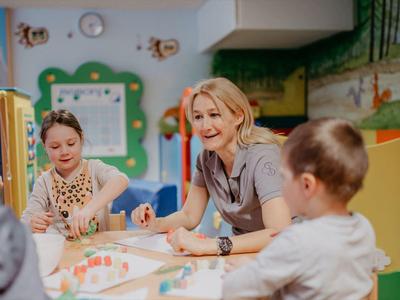 Eine Lehrerin sitzt mit Kindern an einem Tisch und malt im Farbenraum.