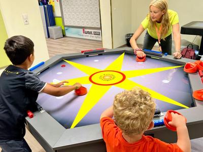 Zwei Kinder spielen Air-Hockey an einem Tisch mit gelbem Sternmuster.