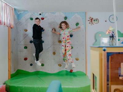 Zwei Kinder springen fröhlich auf einem grünen Indoor-Trampolin in einem bunt dekorierten Spielzimmer.