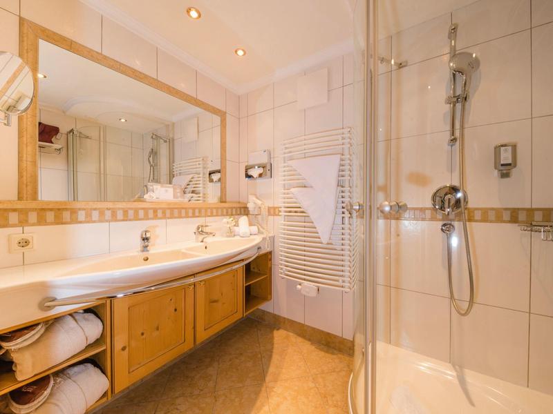 Helles Badezimmer mit Dusche, Doppelwaschbecken und Holzunterschrank in Hotelzimmer.