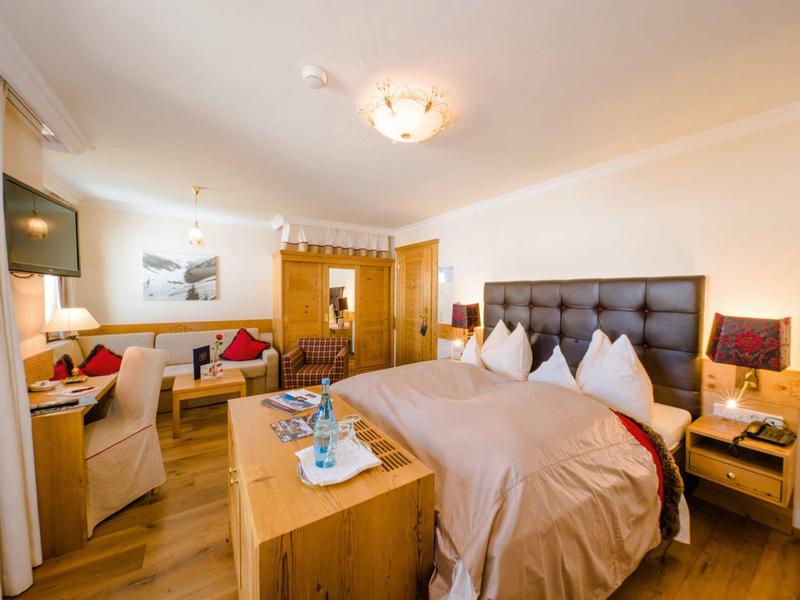 Geräumiges Hotelzimmer mit Doppelbett, Sitzecke, Fernseher und Holzmöbeln in warmem Licht.