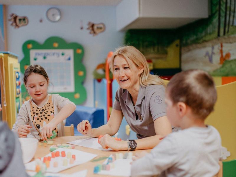 Eine Lehrerin sitzt mit Kindern an einem Tisch und malt im Farbenraum.