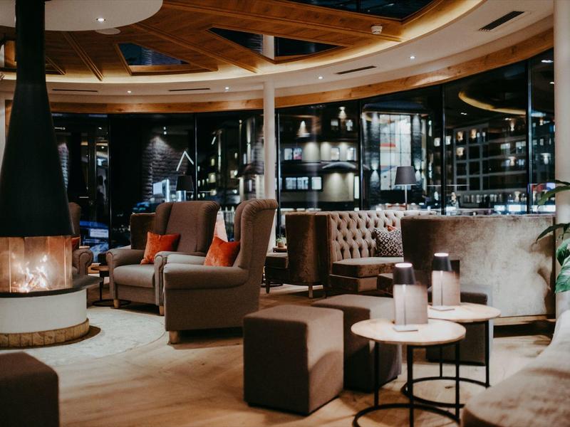 Gemütliche Hotel-Lounge mit modernen Sesseln, Sofas und einem runden Kamin im Zentrum.