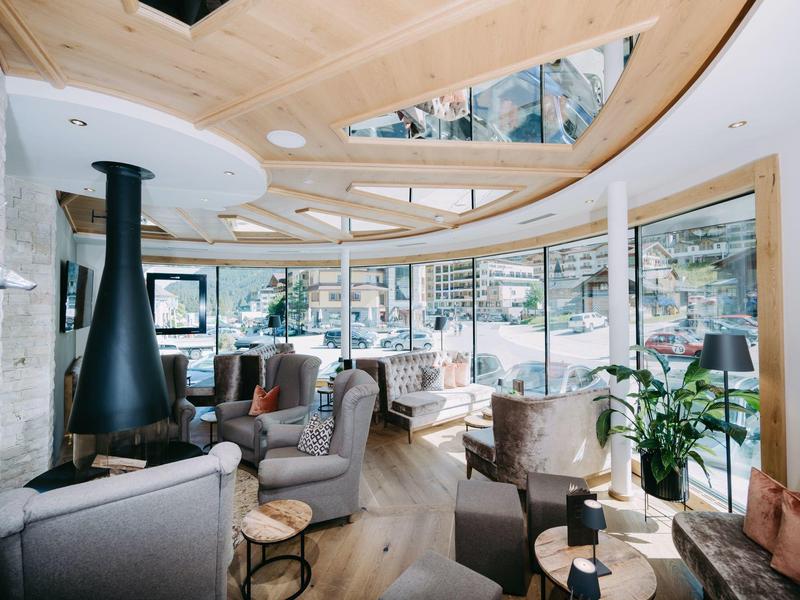 Modernes Hotelzimmer mit Holzbalkendecke, gemütlichen Sesseln und großen Fenstern mit Bergblick.