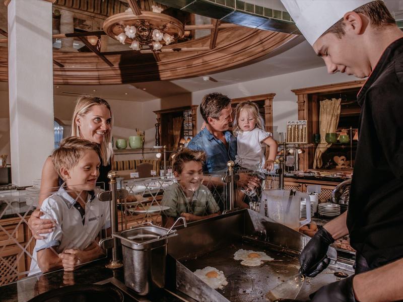 Koch bereitet Speisen vor, während eine Familie in einem Restaurant gerne zuschaut.