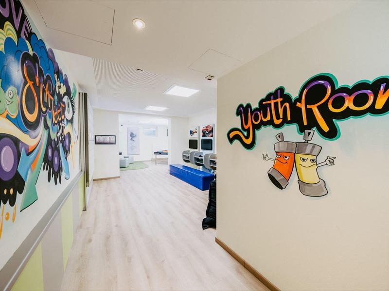 Heller Flur mit moderner Kunst und Beschilderung zum Jugendzimmer in einem Hotel.