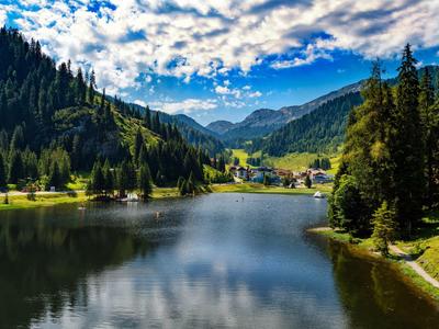 Bergsee mit umliegenden Wäldern und Bergen unter bewölktem blauem Himmel