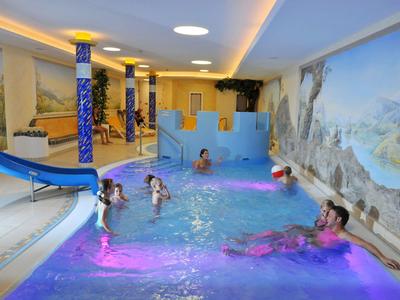 Hallenbad mit Rutsche, mehreren Kindern und Wandgemälde im Hintergrund.